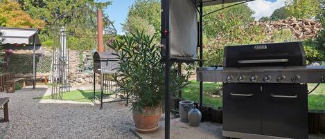 En udendørs terrasse med grill, pergola med tag og en potteplante.