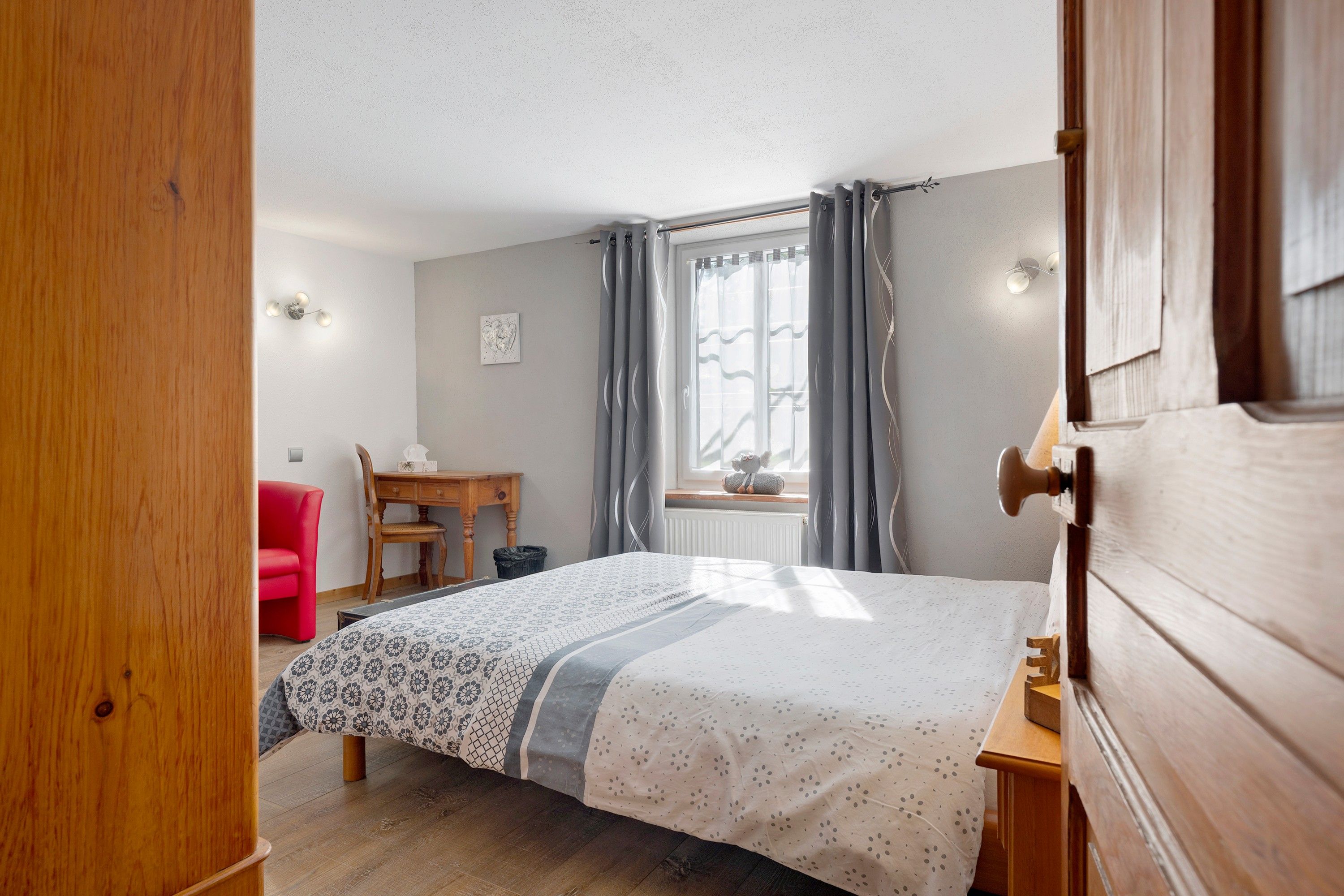 Ein Schlafzimmer mit einem Bett, einem Schreibtisch, einem Stuhl und einem Fenster mit Vorhängen.