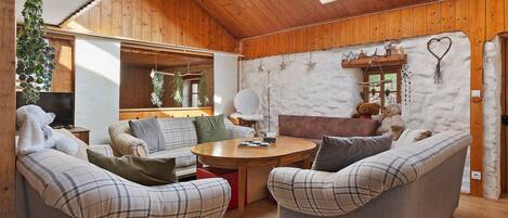 Ein gemütliches Zimmer mit Holzwänden, einer hohen Decke und einem Oberlicht. Ein runder Holztisch mit Stühlen und ein Weihnachtsbaum sind vorhanden.