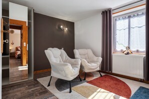 Ein modernes Wohnzimmer mit zwei bequemen Sesseln, einem großen Fenster mit Vorhängen, einer Heizung und einem farbenfrohen Teppich.