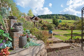 A garden with a stone wall, a wooden birdhouse, and a metal pot. - Guesthouse “Chambre Suite Mansio” with Shared Terrace, Garden & Wi-Fi (Gerbépal)