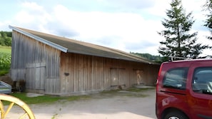 A large wooden barn with a sloped roof, a red vehicle parked nearby, and a tree in the background.