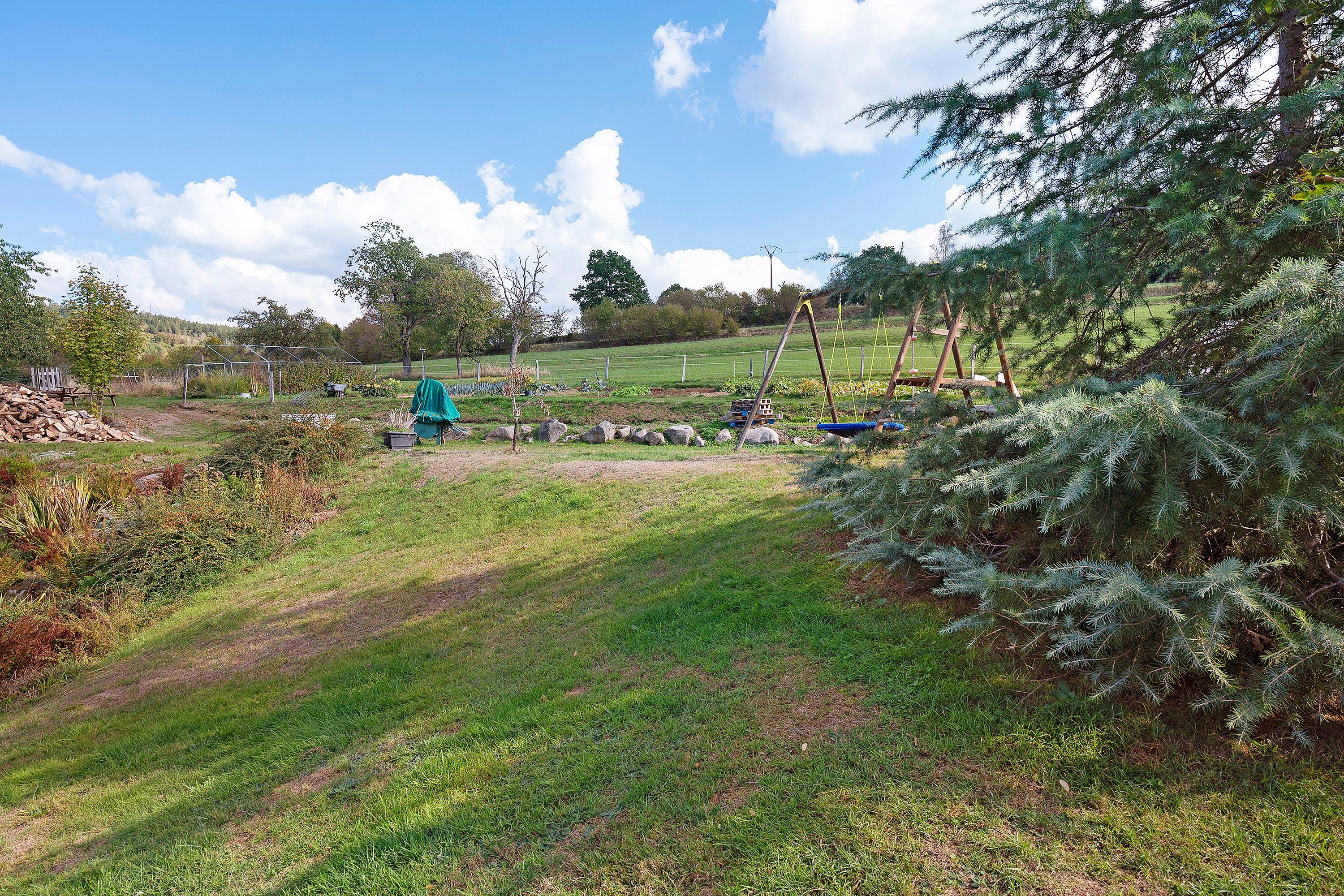 A rural landscape with a garden, a swing set, and a wooden fence.