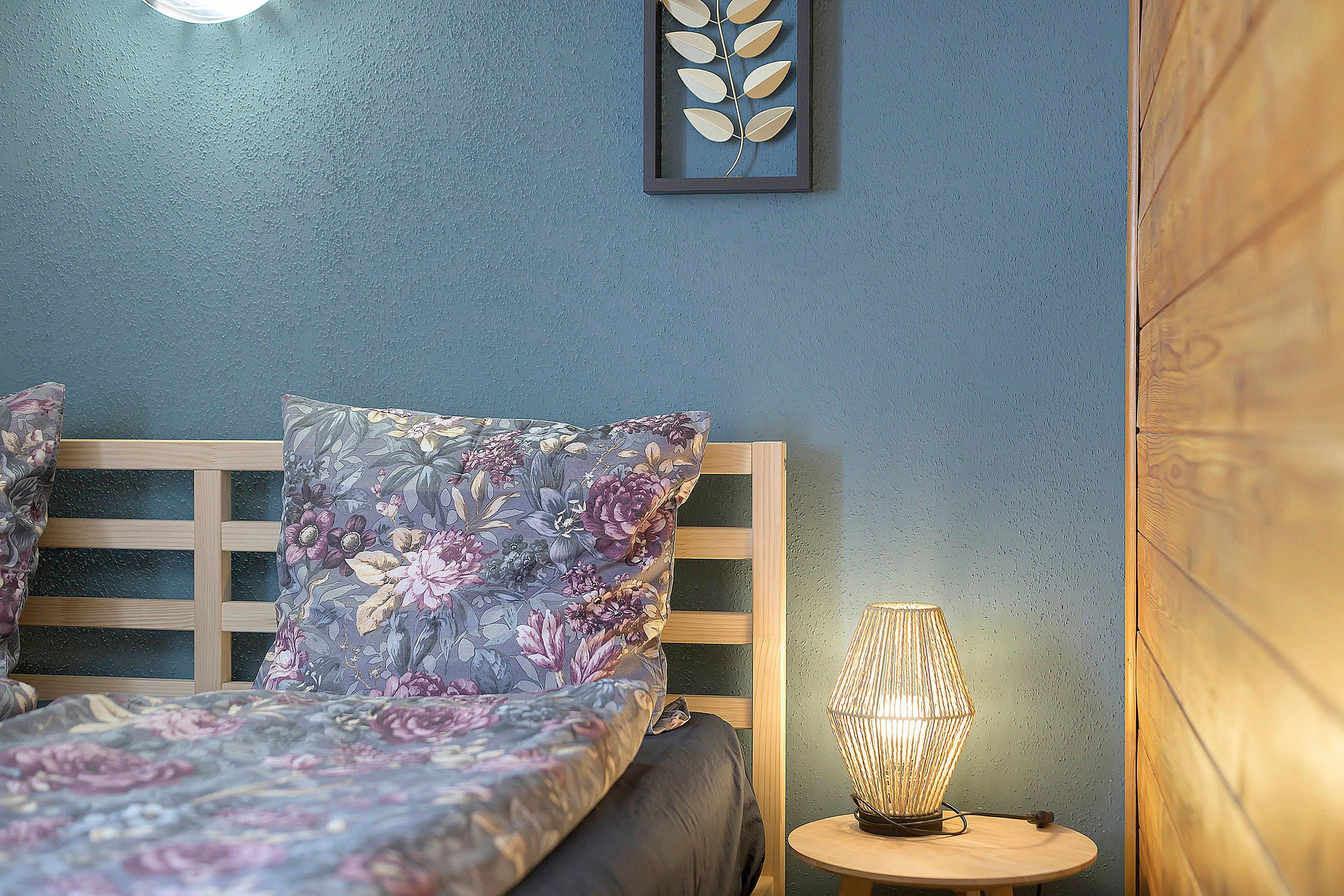 A bedroom with a bed, a nightstand, a wall-mounted light fixture, and a framed leaf decoration.