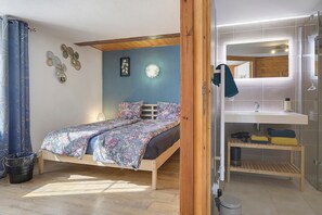 Ein Schlafzimmer mit Bett, Holz-Kopfteil, Nachttisch, Spiegel und einem Badezimmer mit Dusche und Waschbecken.