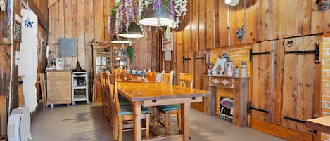 Un intérieur rustique avec des éléments en bois, comprenant une table à manger, des chaises, des suspensions florales et un mur en briques.