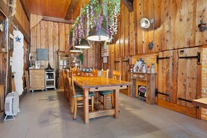 A rustic wooden interior with a dining table, chairs, hanging flower arrangements, and a brick wall. - Guesthouse “Goddess of the Harvest Room” with Shared Terrace, Garden, and Wi-Fi (Gerbépal)