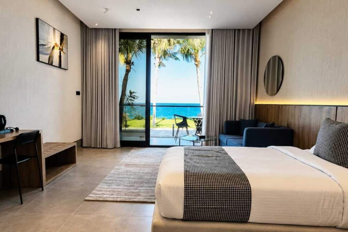 A modern hotel room with a bed, desk, and a view of the ocean.
