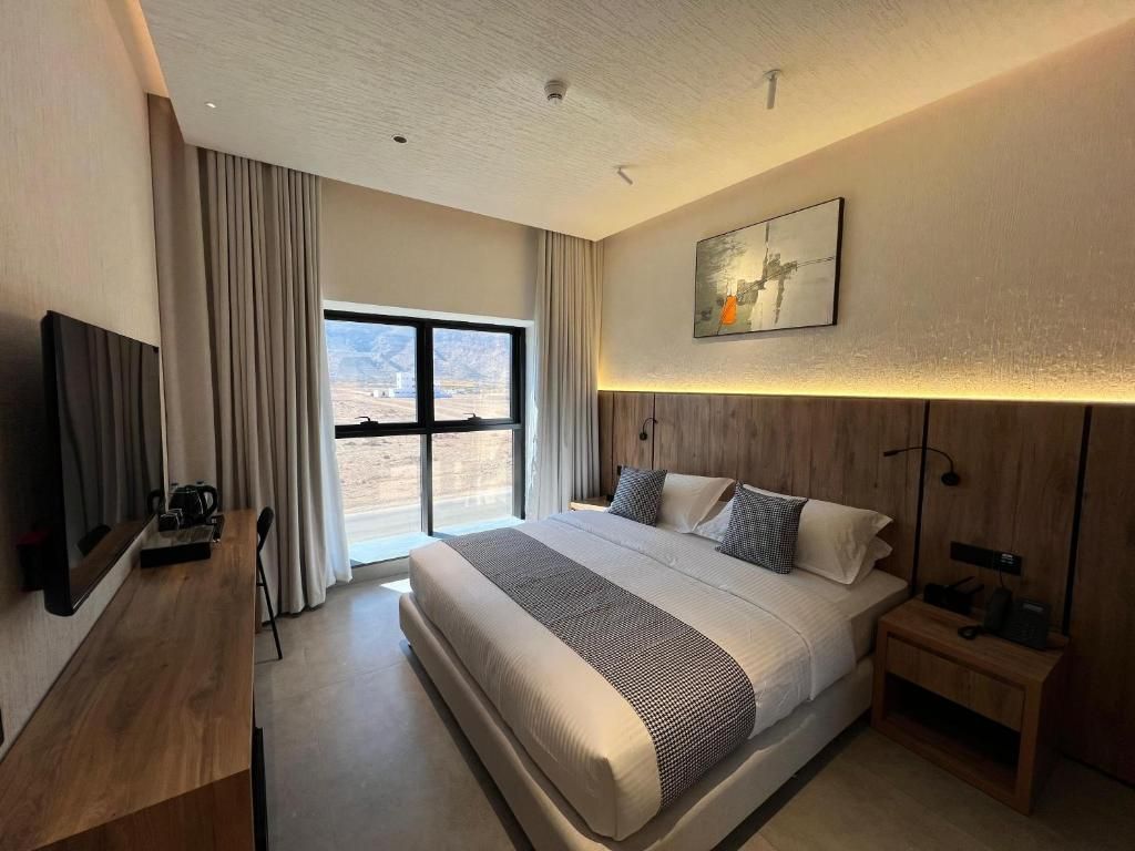 A modern hotel room with a large bed, a flat-screen TV, a desk, and a window with curtains.