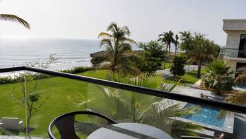 A balcony with a view of the ocean, a swimming pool, and palm trees.