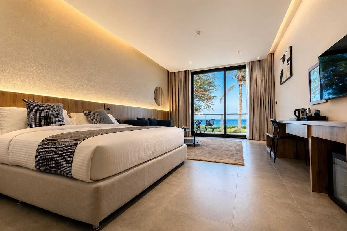 A modern hotel room with a large bed, a desk, a television, and a view of the ocean.