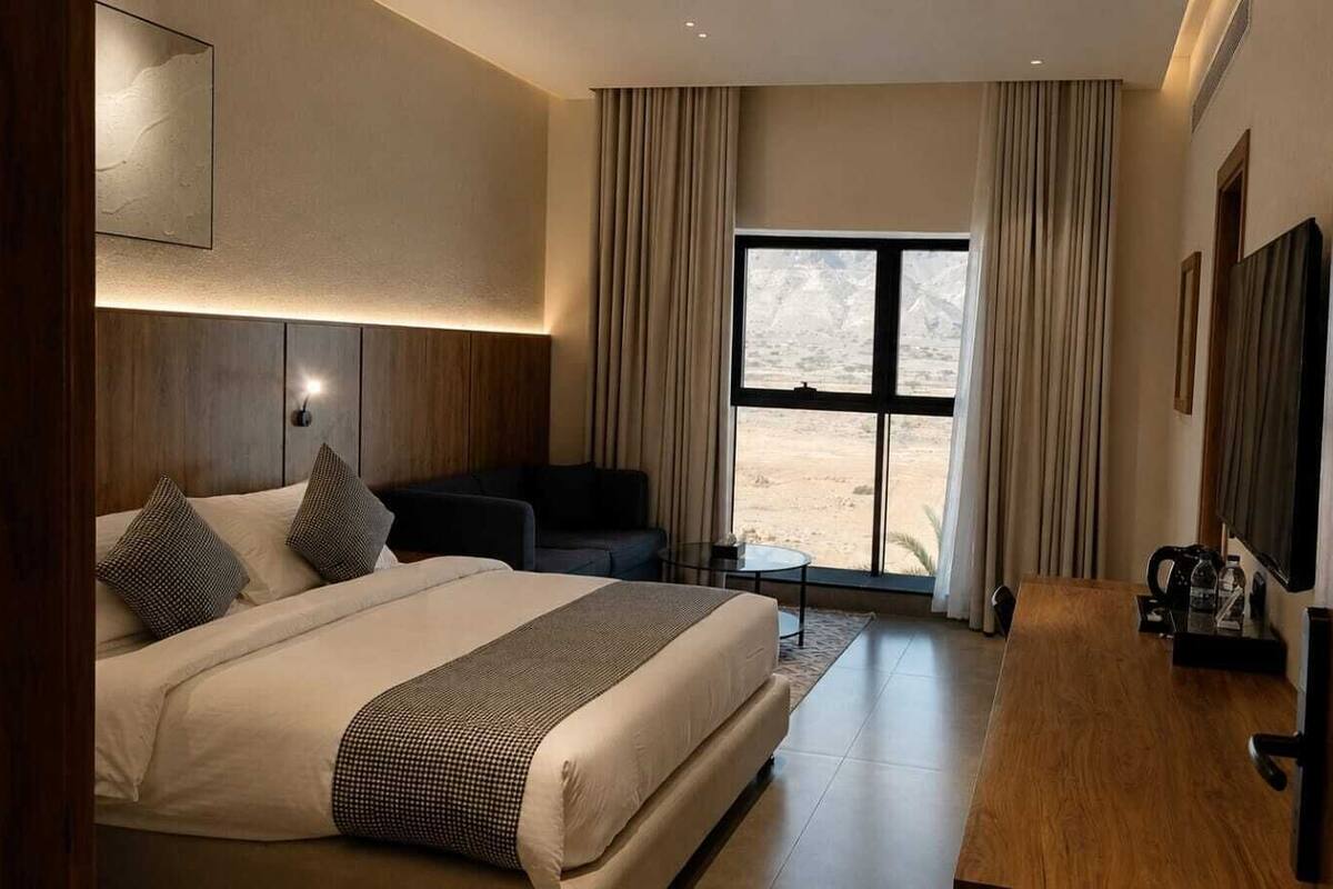 A hotel room with a bed, a desk, a chair, a TV, and a large window with a view.
