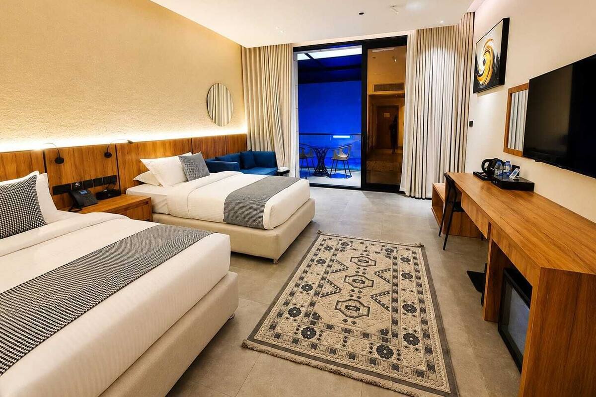 A hotel room with two beds, a desk, a TV, and a balcony with curtains.