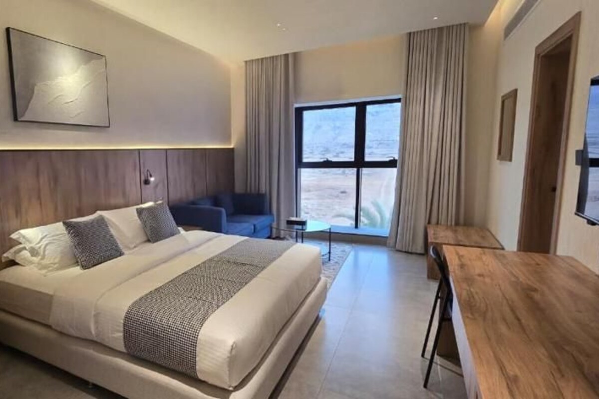 A modern hotel room with a large bed, a desk, and a view of the beach.