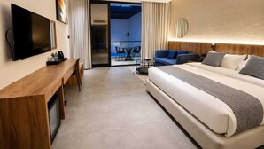 Una habitación de hotel moderna con una cama grande, un escritorio con televisor de pantalla plana, un balcón con vistas y un techo bien iluminado.