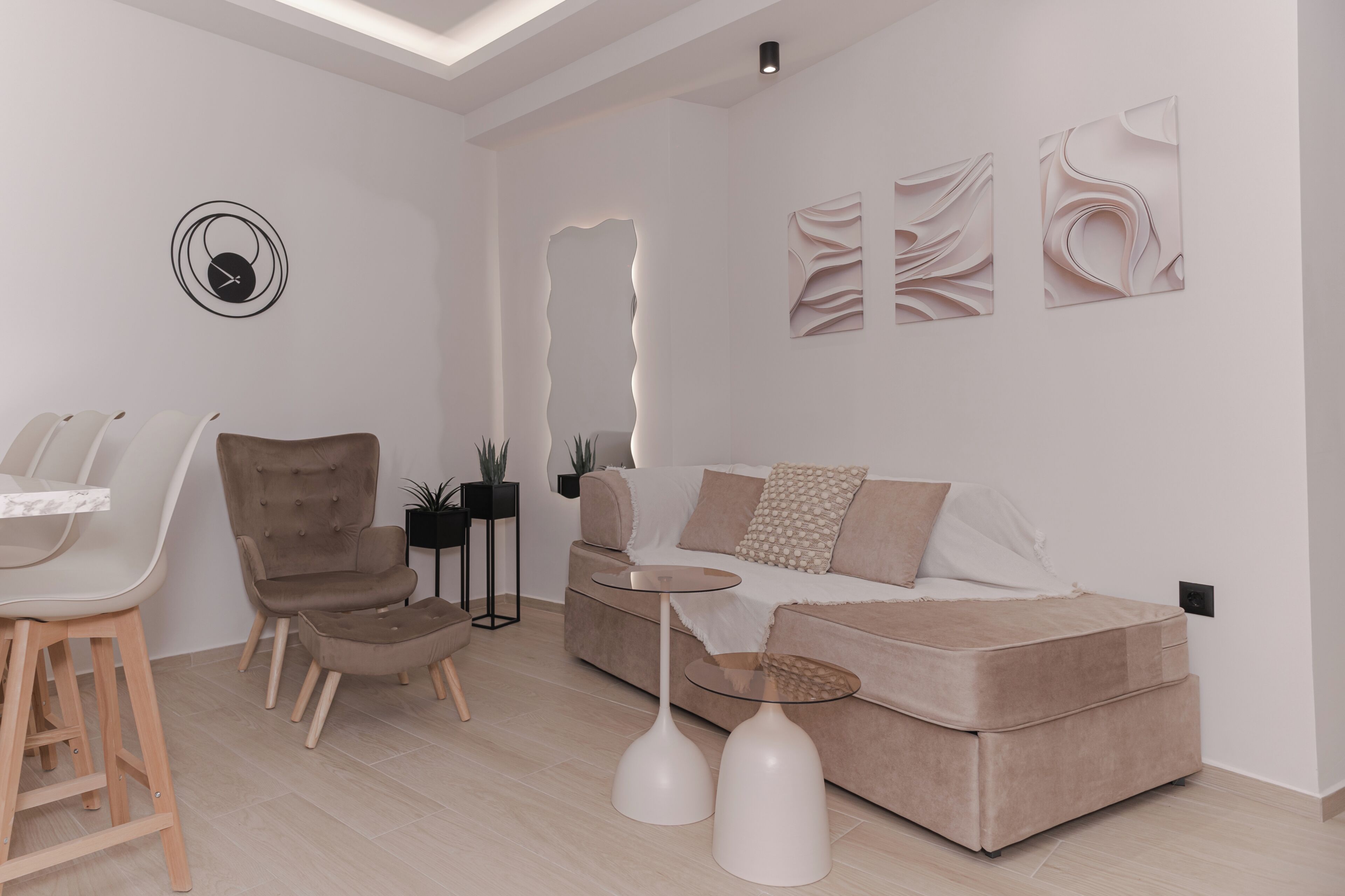 A modern living room with a sofa, chairs, a coffee table, a wall clock, abstract wall art, and a mirror.