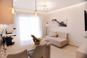 A modern living room with a sofa, a dining table with chairs, a fruit bowl, and a painting on the wall.