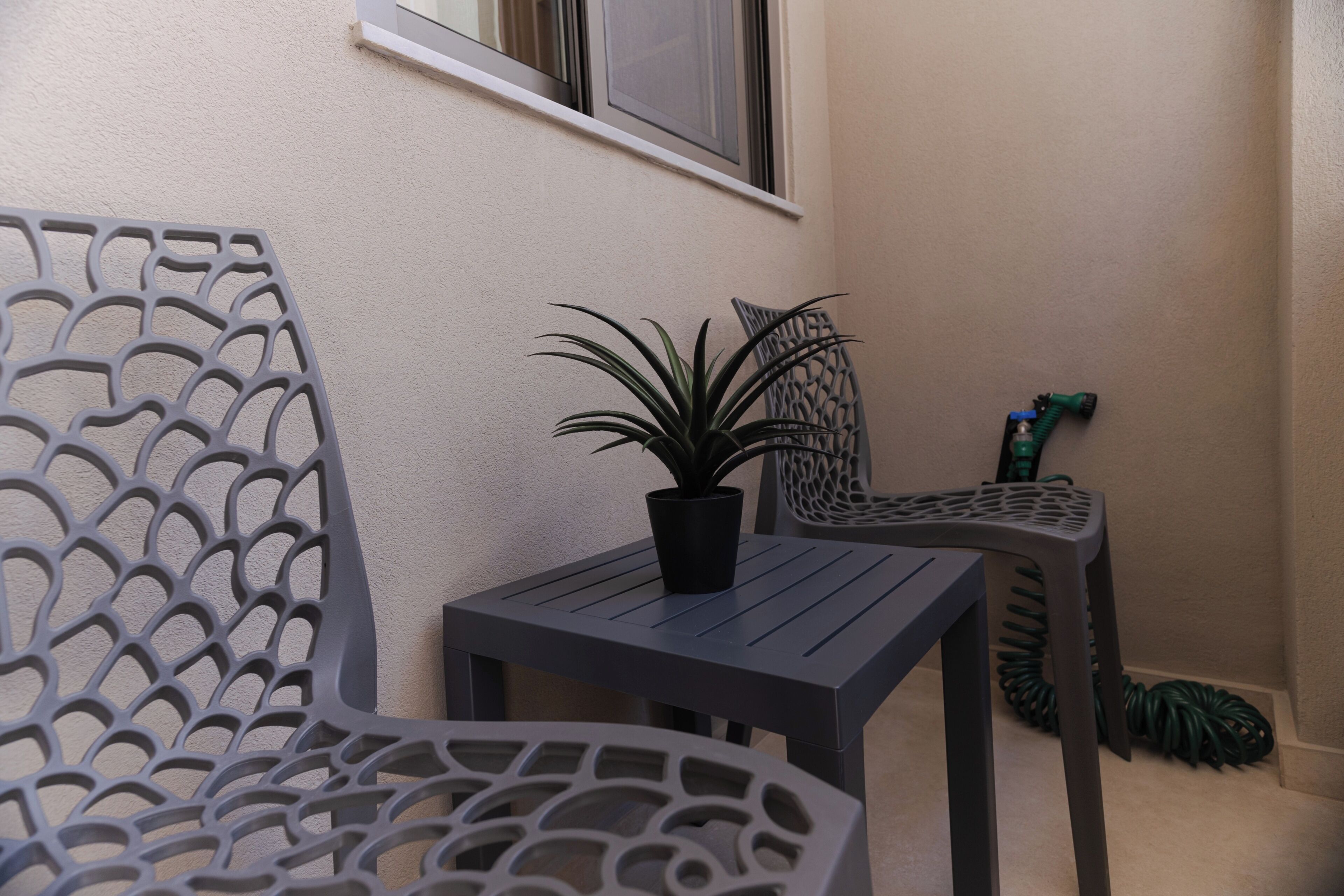 Un balcone con una pianta in vaso, due sedie di metallo e un tavolino.
