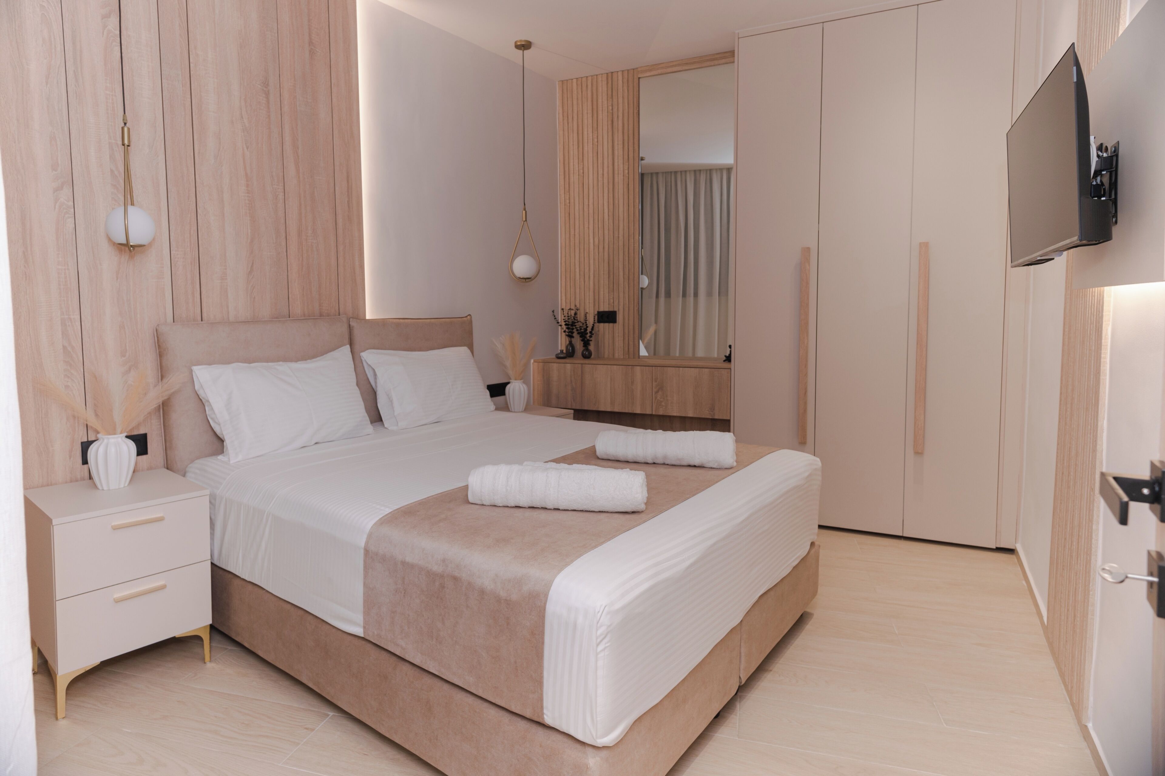A modern bedroom with a large bed, bedside tables, a mirror, and a TV mounted on the wall.