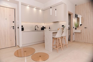 A modern kitchen with white cabinetry, a dining area with two stools, and a small round table.