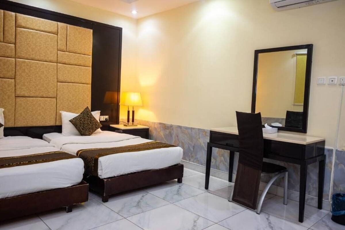 Quarto de hotel com duas camas, uma escrivaninha, uma cadeira, um abajur, um espelho e ar condicionado fixado na parede.
