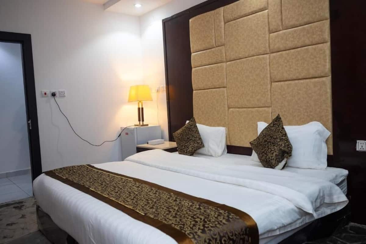 Quarto de hotel com uma cama grande, uma mesa de cabeceira, uma luminária e um painel fixado na parede.