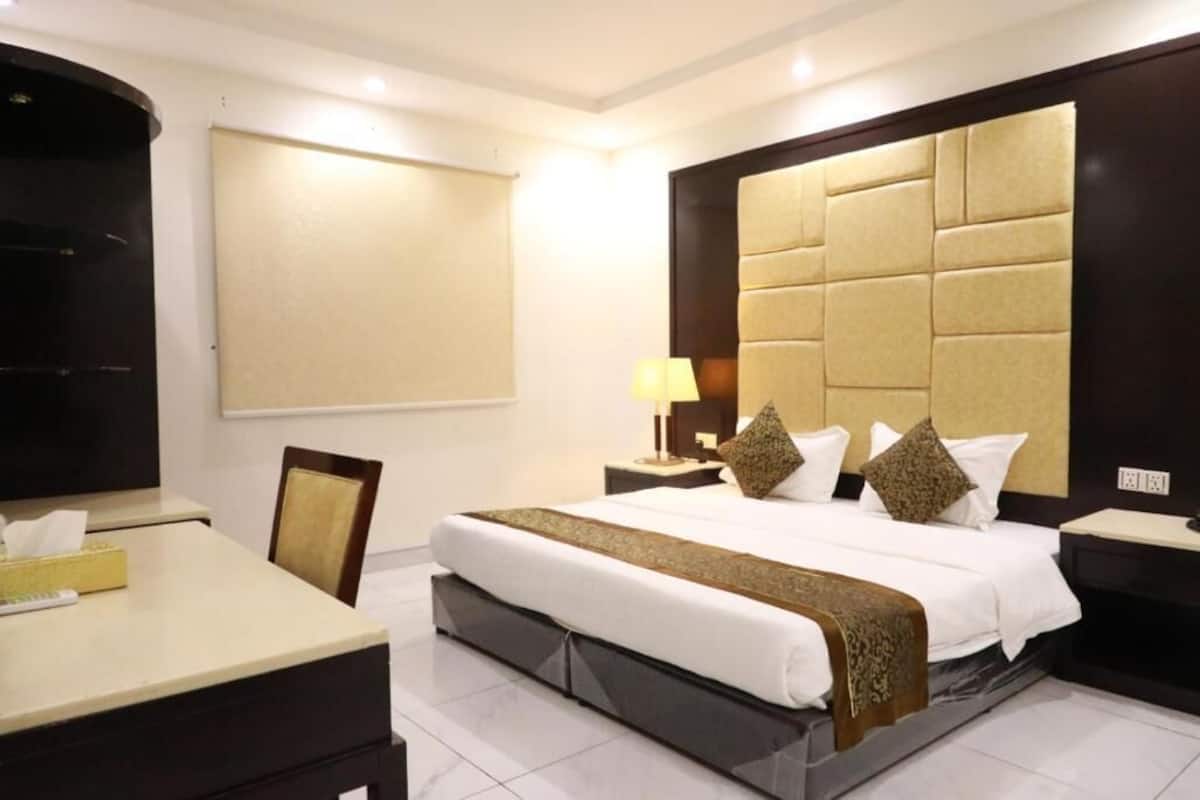 Quarto de hotel com cama, mesas de cabeceira, escrivaninha, cadeira, televisão e uma janela grande.