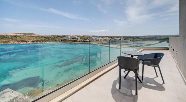 A balcony with a glass railing overlooking a clear blue sea, two chairs, and a table. - Qawra Sea View Penthouse Near Beach (San Pawl il-Baħar)
