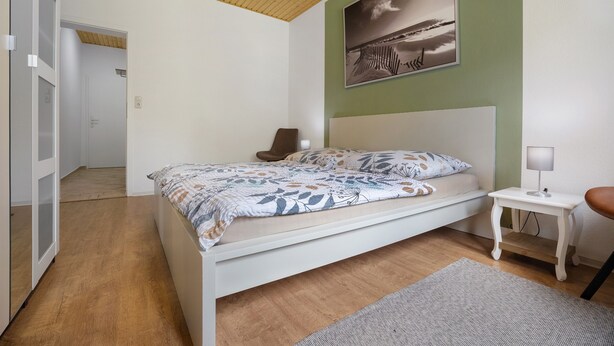 A bedroom with a bed, a bedside table, a lamp, and a picture on the wall. - Holiday Apartment for 6 People (83 m²) in Redefin (Redefin)