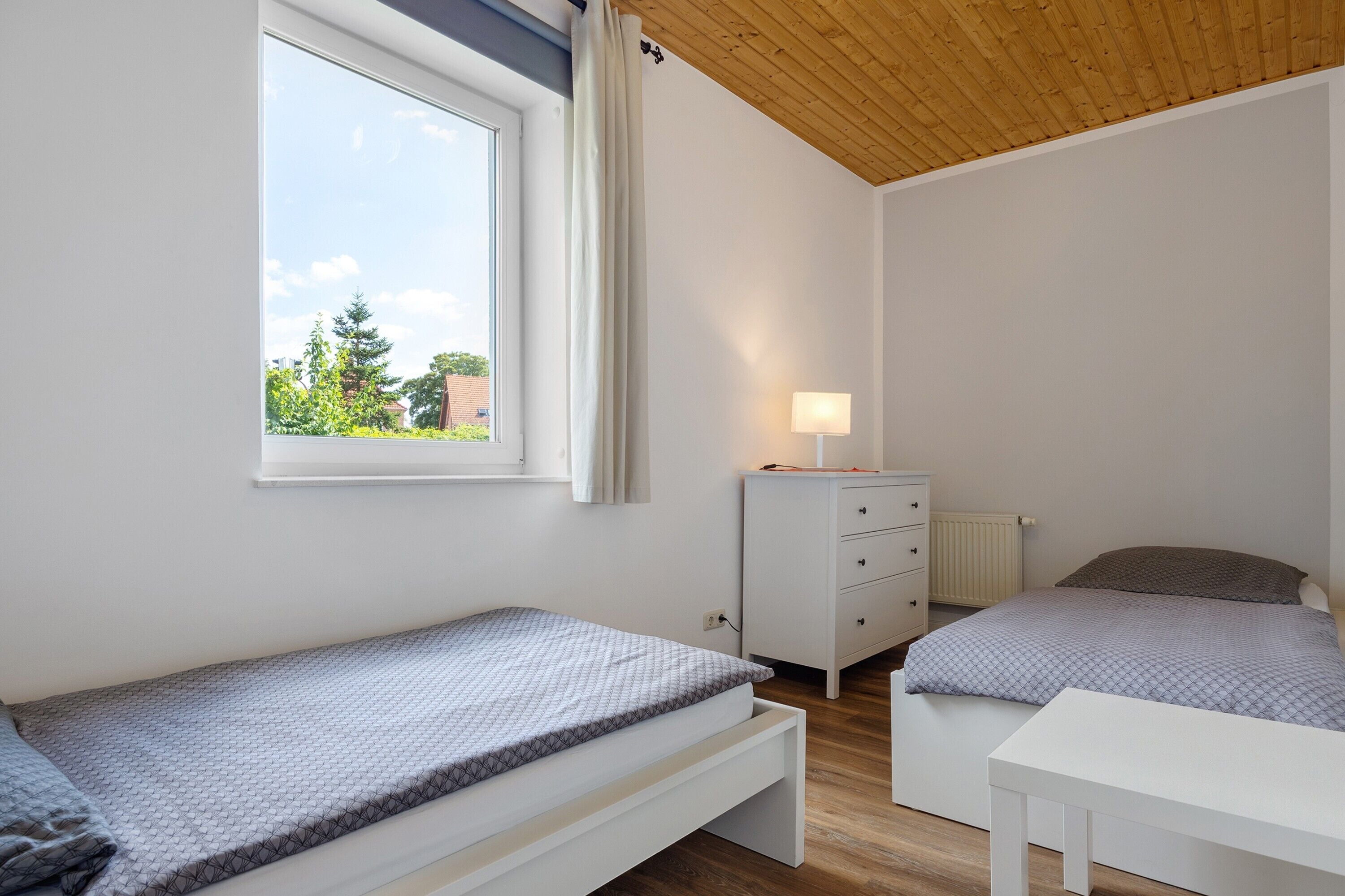 Ein Schlafzimmer mit zwei Betten, einer weißen Kommode, einem Nachttisch und einem Fenster mit Vorhängen.