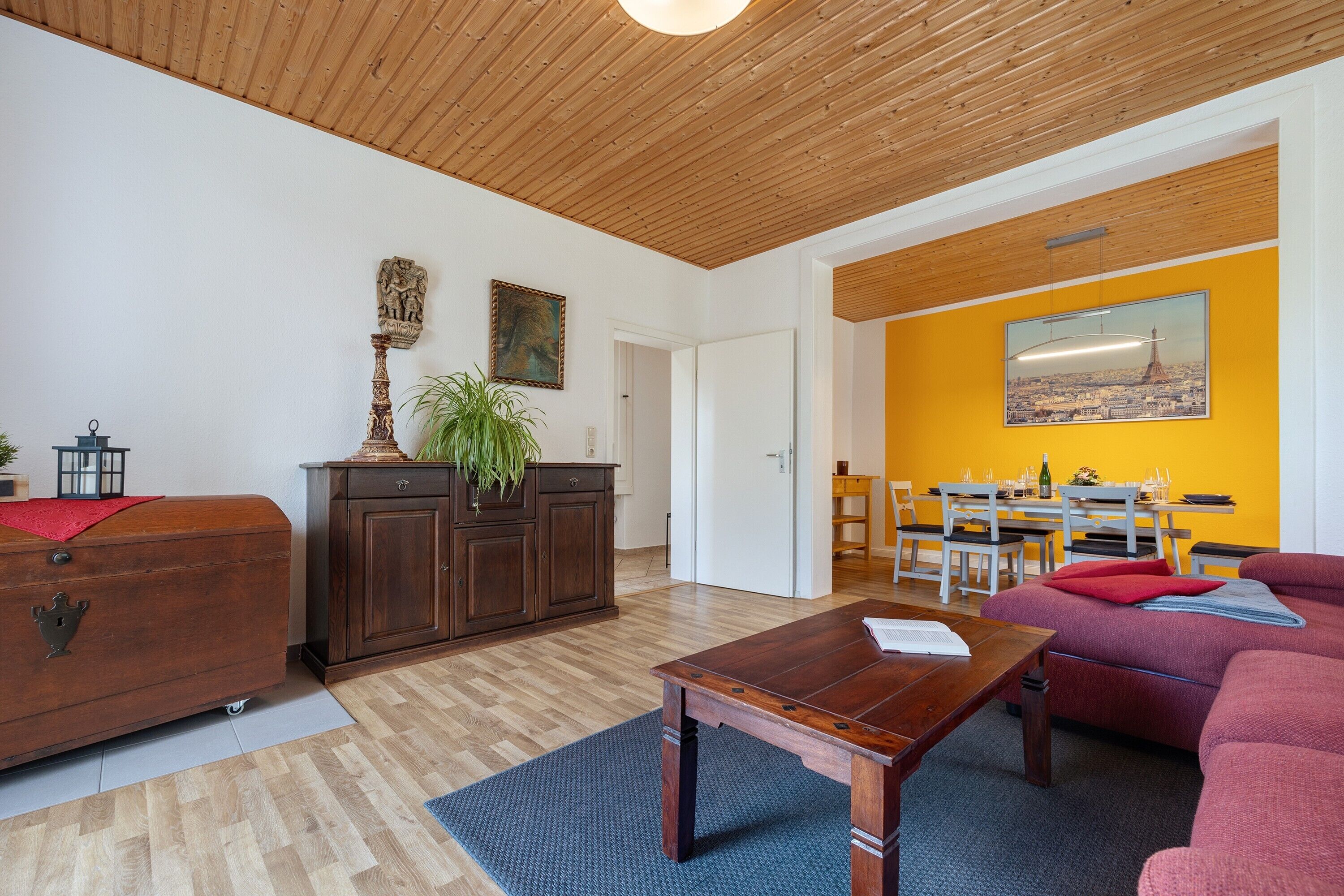 En stue med træloft, sofa, sofabord, skab og spiseområde med bord og stole.