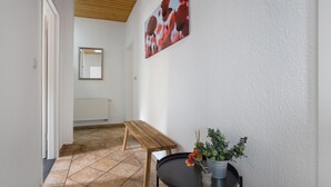 A hallway with a wooden ceiling, a bench, a table with a vase of flowers, and a painting on the wall. - Holiday Apartment for 6 People (83 m²) in Redefin (Redefin)