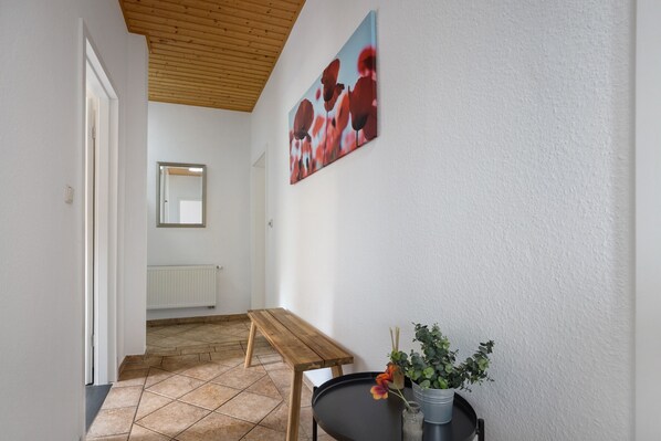A hallway with a wooden ceiling, a bench, a table with a vase of flowers, and a painting on the wall. - Holiday Apartment for 6 People (83 sqm) in Redefin (Redefin)