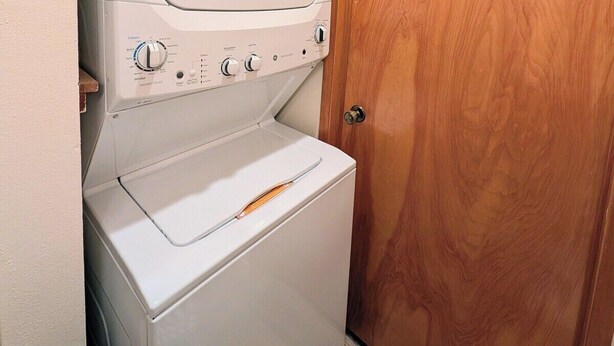 Una lavadora y secadora apiladas en un cuarto de lavado con puerta de madera.