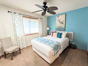 A bedroom with a bed, a chair, a ceiling fan, a window with curtains, and a wall painting. - Turquoise Tide Retreat, Top Floor, Steps to Lake (Chelan)