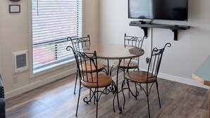 A dining area with a round table, four chairs, a ceiling fan, a wall-mounted TV, and a window with blinds. - Turquoise Tide Retreat, Top Floor, Steps to Lake (Chelan)