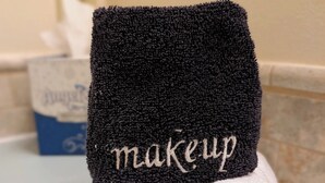 Toalla con el texto 'makeup' bordado, sobre una encimera de baño.