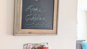 A welcome sign with a rustic wooden frame and chalkboard background, a small metal shelf below holding travel guides, and a light switch on the wall.