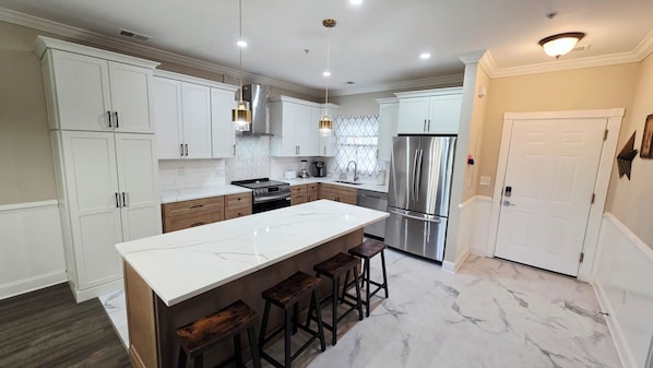 A modern kitchen with white cabinetry, a large island with stools, stainless steel appliances, and a marble floor.