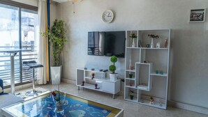 Un salon moderne avec une table basse en verre, un téléviseur à écran plat, un meuble de rangement blanc et une plante en pot.