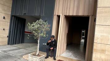 Un homme est assis devant un bâtiment, avec un pot de fleurs à proximité.