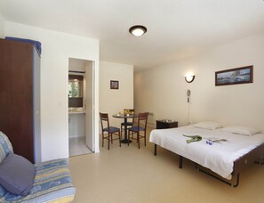 A bedroom with a bed, a desk with chairs, a small table with fruits, a telephone, and a picture on the wall. - Trio Retreat in Vallon-pont-d'arc (Vallon-Pont-d'Arc)
