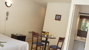 Quarto de hotel com uma cama, uma mesa com cadeiras, um telefone e um quadro na parede.