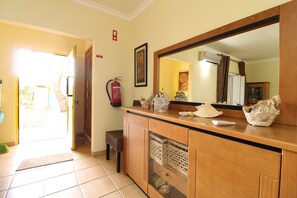 A room with a wooden cabinet, a large mirror, a fire extinguisher, and a door leading outside. - Real Village (Faro)