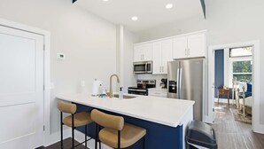 A modern kitchen with white cabinets, stainless steel appliances, and a central island with bar stools. - The Bavarian Inn 4 Chic Stay (Covington)