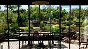 Ein Essbereich mit Holztisch, Stühlen und Blick auf einen üppigen Garten durch große Fenster.