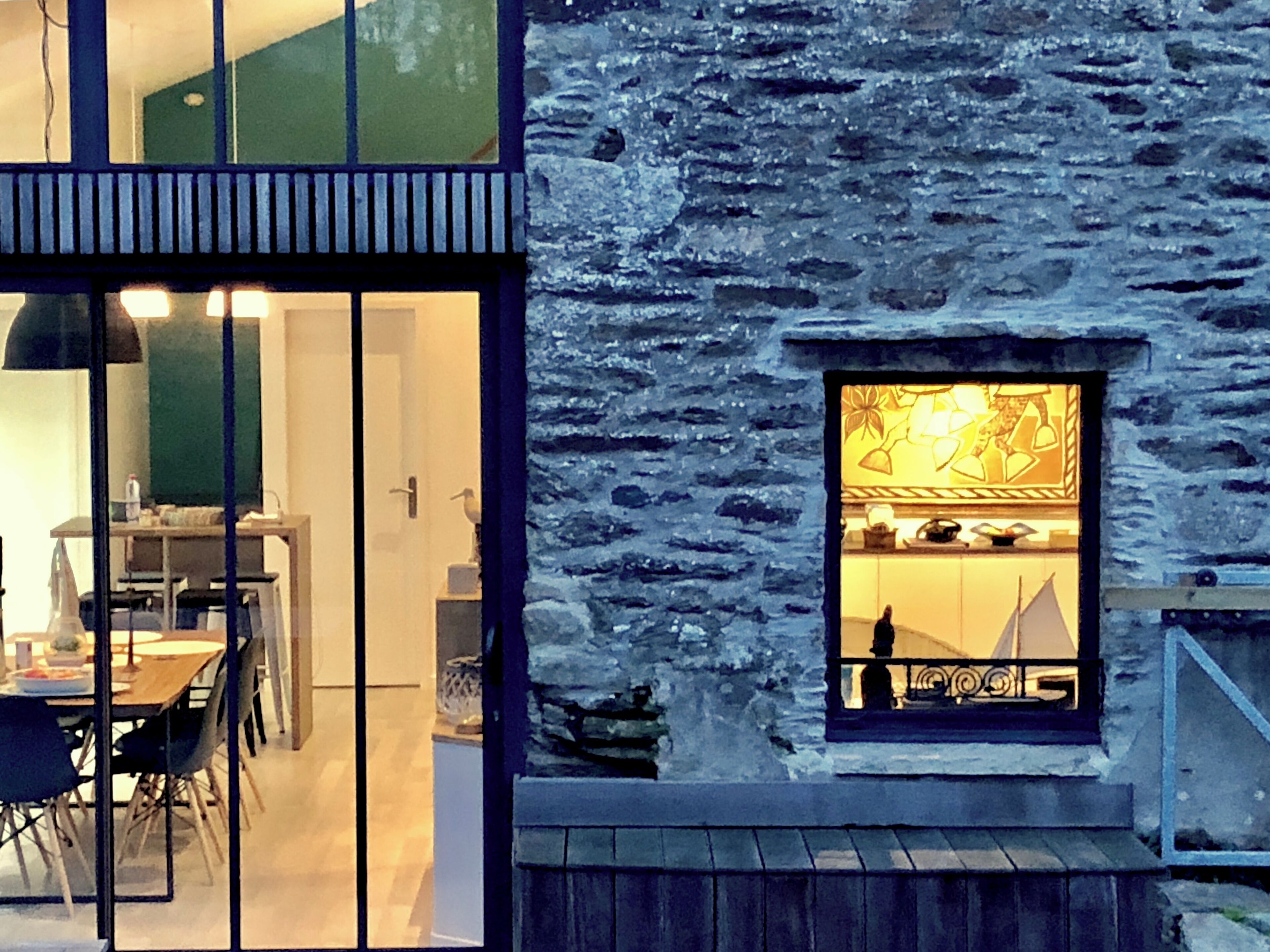 A modern building with a stone facade, a dining area with chairs and a table, and a view of a sailboat through a window.