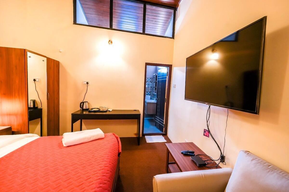 A hotel room with a bed, a desk, a TV, and a balcony.