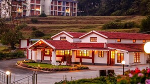 A hotel with a red-tiled roof, multiple windows, and a well-lit entrance. - Lauriston Villa Ooty by VOYE HOMES (Ooty)