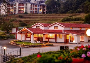 A hotel with a red-tiled roof, multiple windows, and a well-lit entrance. - Lauriston Villa Ooty by VOYE HOMES (Ooty)